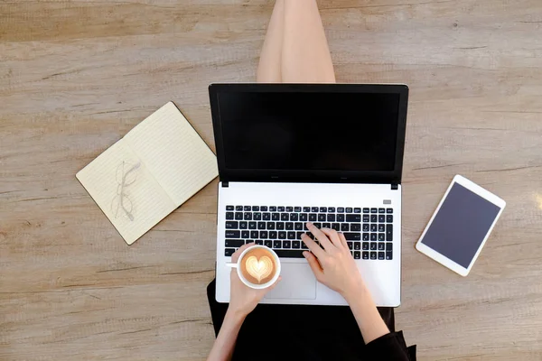 Siyah elbiseli genç bir kadının ahşap zeminde oturup dizüstü bilgisayarı üzerinde çalışmasının en iyi görüntüsü. Dişi ayağının kesilmiş hali. Kapat, kopyala boşluk, arkaplan.