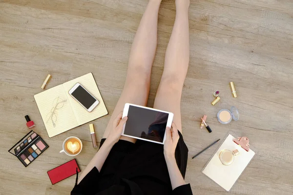 Siyah elbiseli genç bir kadının ahşap zeminde oturup tablet bilgisayarını tutuşu. Dişi ayağının kesilmiş hali. Kapat, kopyala boşluk, arkaplan.