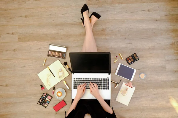 Top view of young woman wearing black dress sitting on wooden floor and working on her laptop. Cropped shot of female\'s feet. Close up, copy space, background.