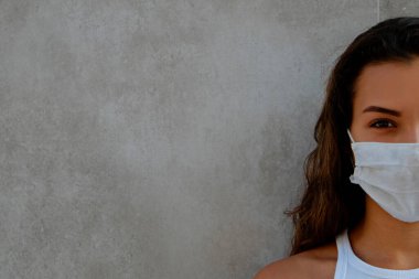 Beton duvarın yanında duran bulaşıcı maddelerden korunmak için tek kullanımlık maske takan Arap kökenli genç bir kadının portresi. Kapat, kopyala boşluk, arkaplan.