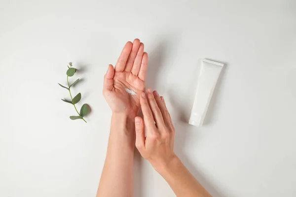 Revitalizing hand cream for healing and recovery after excessive use of soap and disinfectants. Young woman applying moisturizing lotion. Copy space, close up, pink background, flat lay, top view.