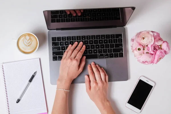 Beyaz dizüstü bilgisayarda çalışan, masa arkası desenli bir kadının en iyi görüntüsü. Çiçek buketli kadınsı çalışma alanı. Kapat, boşluğu kopyala.