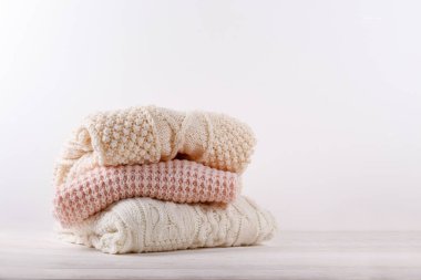 Beyaz ahşap masa üzerine yığılmış farklı örgü desenleri olan pastel renkli bir sürü süveter örülmüş. Sonbahar mevsimi örgü. Kapat, metin için boşluk kopyala