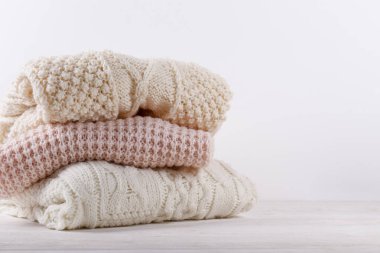 Beyaz ahşap masa üzerine yığılmış farklı örgü desenleri olan pastel renkli bir sürü süveter örülmüş. Sonbahar mevsimi örgü. Kapat, metin için boşluk kopyala