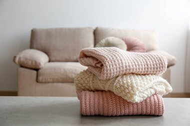 Masada temiz, yeni yıkanmış, düzgünce katlanmış kadın giysileri yığını var. Masada bir yığın gömlek, elbise ve süveter, beton duvar arkaplanı. Boşluğu kopyala, kapat, üst görünüm.