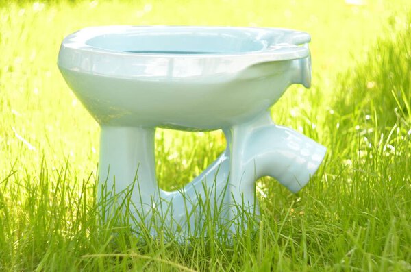 Туалет сделан в СССР в белом цвете. Вид с левой стороны на фоне зеленой травы в солнечный день
.