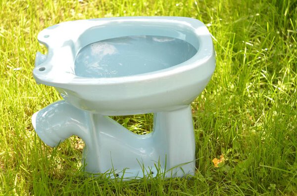 Туалет сделан в СССР в белом цвете. Вид сверху с правой стороны на фоне зеленой травы в солнечный день
.