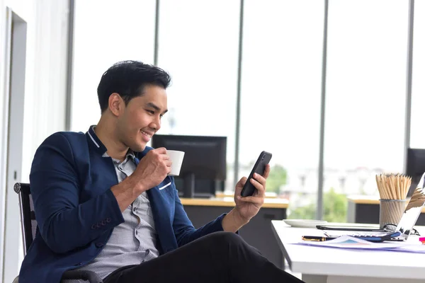 Young Asian Businessmen Watch Smart Phones Hold Coffee Mugs Work — Stock Photo, Image
