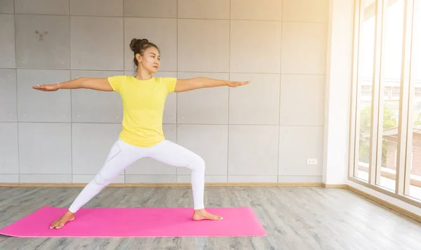 Stüdyoda spor giyerek yoga yapan güzel Asyalı genç bir kadın. Doğal ışık. Konsept: yoga yeni başlayanlar için poz verir..