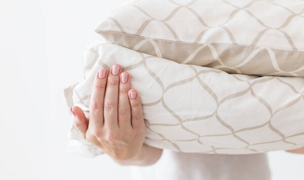 Руки женщины, держащей современные бежевые постельное белье кучу, белый фон стены в тренде, минимализм чистой концепции дома
