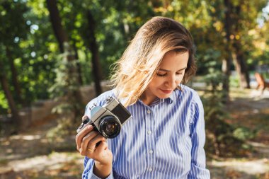 Şık giyim Sonbahar Park vintage fotoğraf makinesi, yaratıcı profesyonel kadın photographre güneşli gün boyunca fotoğraf yapma kullanarak fotoğraf çekmek sevimli gülümseyen genç kadın. Seçici odak