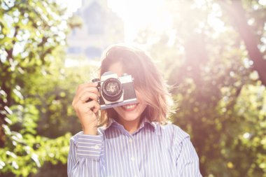 Şık giyim Sonbahar Park vintage fotoğraf makinesi, yaratıcı profesyonel kadın photographre güneşli gün boyunca fotoğraf yapma kullanarak fotoğraf çekmek sevimli gülümseyen genç kadın. Seçici odak
