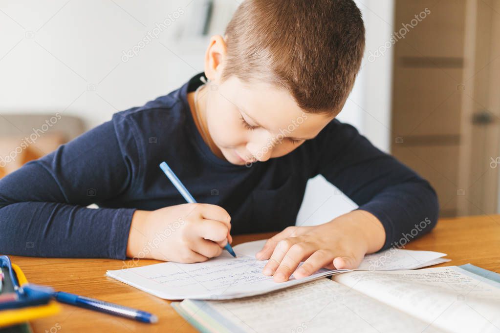 Schoolboy doing his maths homework in ukrainian language on desk at home. Homeschooling concept