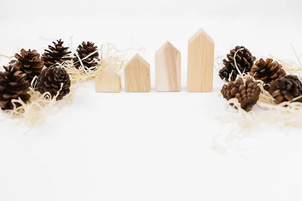 Lined up set of pinecones on wood shavings and wooden blocks house shape. Real estate sale and price increase concept, copy space. Holiday time