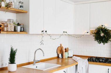 Beyaz modern mutfak İskandinav tarzı Noel için dekore edilmiştir. Şık şık beyaz seramik tuğla duvar, açık ahşap raflar, ahşap masa üstü