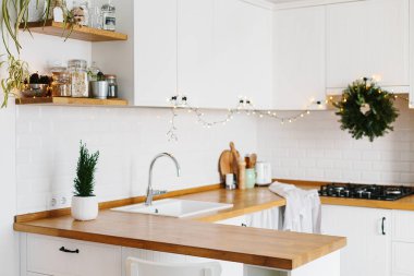 Beyaz modern mutfak İskandinav tarzı Noel için dekore edilmiştir. Şık şık beyaz seramik tuğla duvar, açık ahşap raflar, ahşap masa üstü