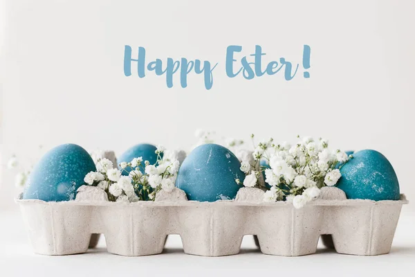 Blue natural colored easter eggs in tray with small white flowers baby breath gypsophila. Happy Easter word