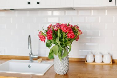 Lale buketi vazo daimi mutfak ahşap tezgah üzerinde. İskandinav tarzı modern beyaz mutfak u şeklinde.