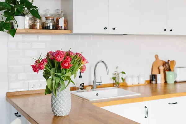 Ramo de tulipanes en jarrón de pie sobre encimera de madera en la cocina. Moderna cocina blanca en forma de u en estilo escandinavo . — Foto de Stock