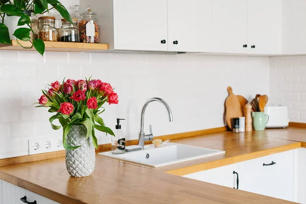 Lale buketi vazo daimi mutfak ahşap tezgah üzerinde. İskandinav tarzı modern beyaz mutfak u şeklinde.