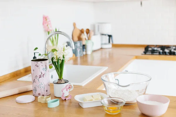 Backzutaten auf Holztisch gelegt, fertig zum Kochen. Konzept der Essenszubereitung, weiße Küche im Hintergrund. — Stockfoto