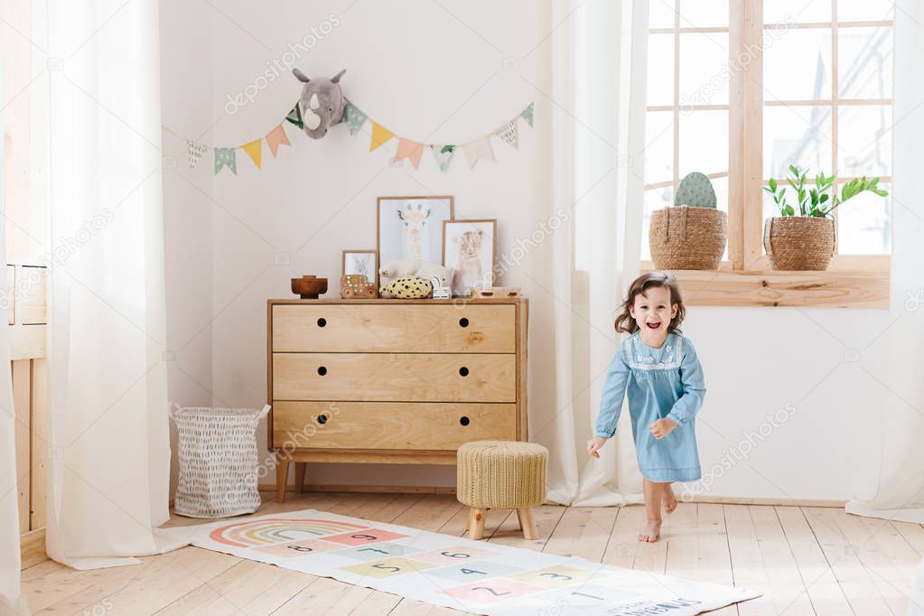 Little girl wearing light blue dress playing in children room scandinavian style.