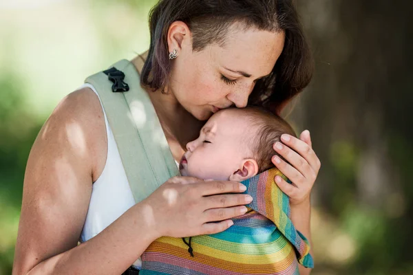 Informal mother carry baby girl in baby carrier in park — Stock Photo, Image