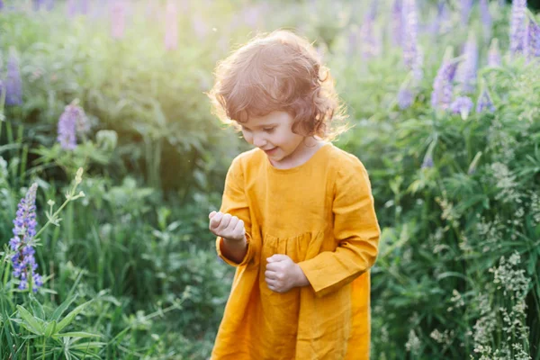 Adorável menina vestindo vestido de linho de mostarda com joaninha entre flores de tremoço — Fotografia de Stock