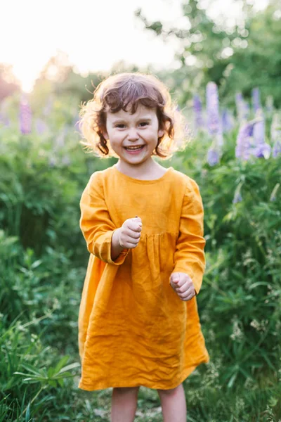 Чарівна дівчинка в гірчичній лляній сукні з сонечком серед квітів люпину — стокове фото