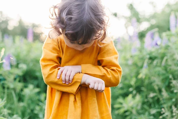 Adorable petite fille portant une robe de lin moutarde avec coccinelle parmi les fleurs de lupin — Photo