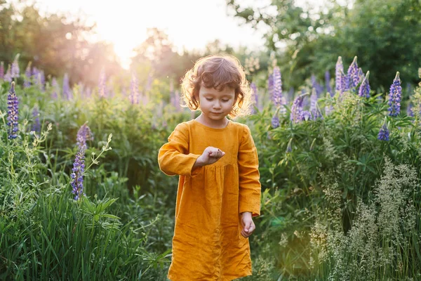 Adorable petite fille portant une robe de lin moutarde avec coccinelle parmi les fleurs de lupin — Photo