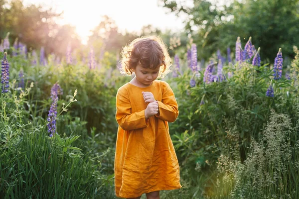 Adorable petite fille portant une robe de lin moutarde avec coccinelle parmi les fleurs de lupin — Photo