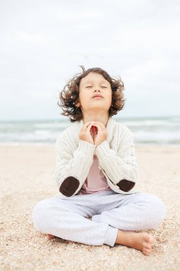 Küçük kız sahilde meditasyon yapıyor, yoga yapıyor, pastel renkler yapıyor.