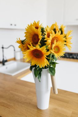 Mutfakta vazoda ayçiçeği buketi, seçici odaklanma. Arka planda İskandinav tarzı temiz, basit, modern bir mutfak.