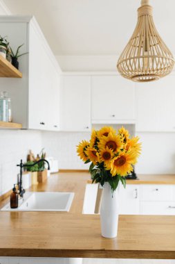 Mutfakta vazoda ayçiçeği buketi, seçici odaklanma. Arka planda İskandinav tarzı temiz, basit, modern bir mutfak.