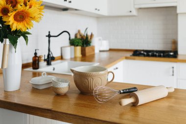 Tabaklar mutfak masasında, yemek yapmaya hazır. İskandinav tarzında beyaz, basit, modern mutfak, mutfak detayları, ahşap masa, masadaki ayçiçeği buketi.
