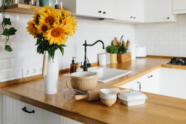 Tabaklar mutfak masasında, yemek yapmaya hazır. İskandinav tarzında beyaz, basit, modern mutfak, mutfak detayları, ahşap masa, masadaki ayçiçeği buketi.