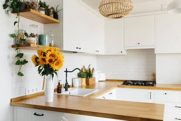 İskandinav tarzında temiz, basit, modern mutfağa bakın. Mutfak detayları, ahşap masa, masadaki ayçiçeği buketi.