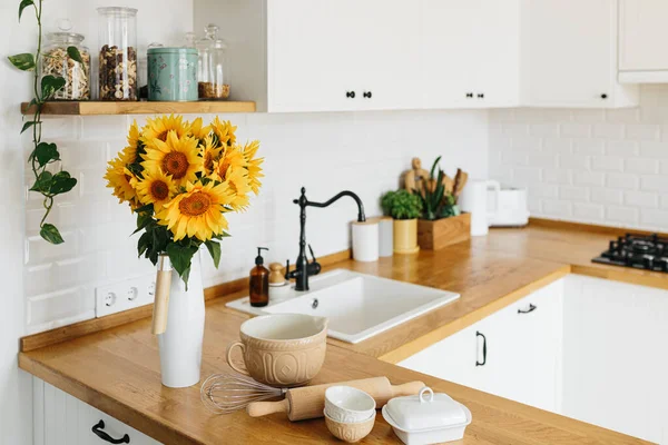 Tabaklar mutfak masasında, yemek yapmaya hazır. İskandinav tarzında beyaz, basit, modern mutfak, mutfak detayları, ahşap masa, masadaki ayçiçeği buketi.