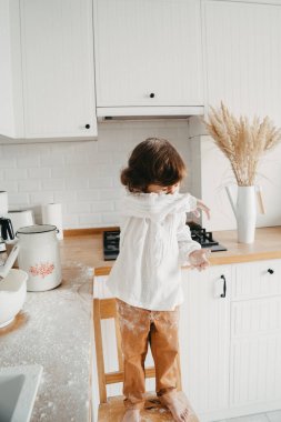 Küçük kız mutfakta krep için hamur hazırlıyor. Yemek hazırlama kavramı, unla eğlenmek. Gerçek hayatta sıradan bir fotoğraf serisi.