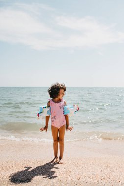 Genç kız pembe mayo giyip tek boynuzlu atlar takıyor ve çocukların yüzme kolluklarını takıyor. Tatil zamanı