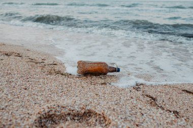 Kıyıda duran plastik evcil hayvan şişesi çevreyi kirletiyor. Kumsalda çöp..