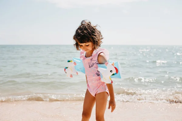 年轻的蹒跚学步的小女孩穿着粉色泳衣 带着独角兽和孩子们在海里游泳的臂章 行动时间 — 图库照片