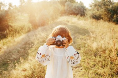 Nakış işlemeli bluz giyen küçük bir kız, eski fotoğraf makinesiyle fotoğraf çekimi yaz günbatımı, pozitif titreşimler, basit kırsal yaşam. Atmosferik resim