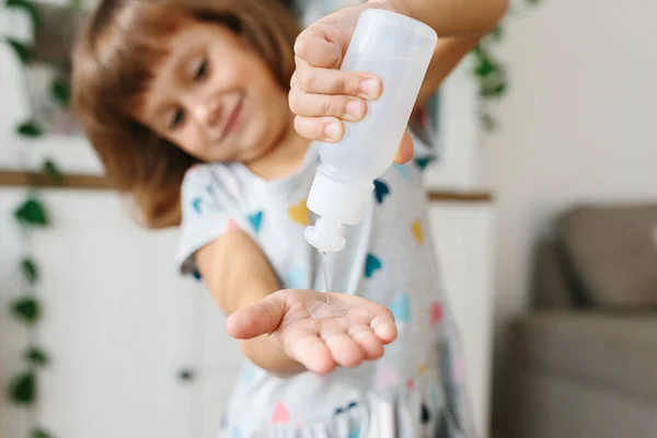Disinfecting hands. Child girl using disinfection alcohol gel on hands home living room background to prevent virus epidemic. Selective focus on sanitizer bottle
