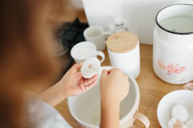 Çocuk kız pişirmek için hamur hazırlıyor - kasede yumurta kırıyor - ev yemeği. Yemek hazırlama kavramı, arka planda beyaz mutfak. Gerçek hayatta sıradan bir fotoğraf serisi.