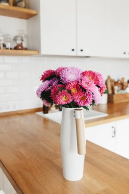 Michaelmas papatyası, vazoda asteroit, seçici odaklanma. Arka planda İskandinav tarzı temiz, basit, modern bir mutfak.