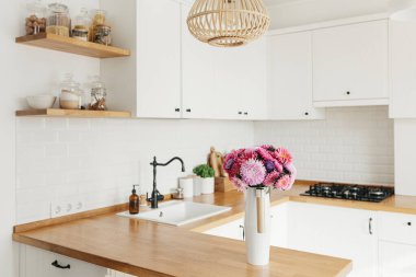 İskandinav tarzında temiz, basit, modern mutfağa bakın. Mutfak detayları, ahşap masa. Masadaki paskalya Michaelmas papatyası.