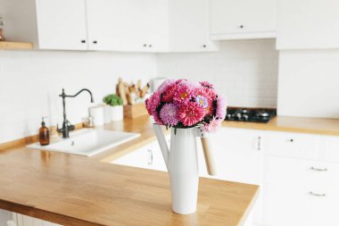 İskandinav tarzında temiz, basit, modern mutfağa bakın. Mutfak detayları, ahşap masa. Masadaki paskalya Michaelmas papatyası.