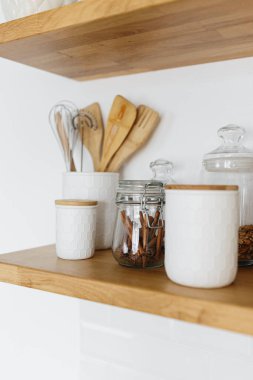 Kitchen shelves with various white ceramic and glass jars. Open shelves in the kitchen. Kitchen interior ideas. Eco friendly kitchen, zero waste home concept clipart